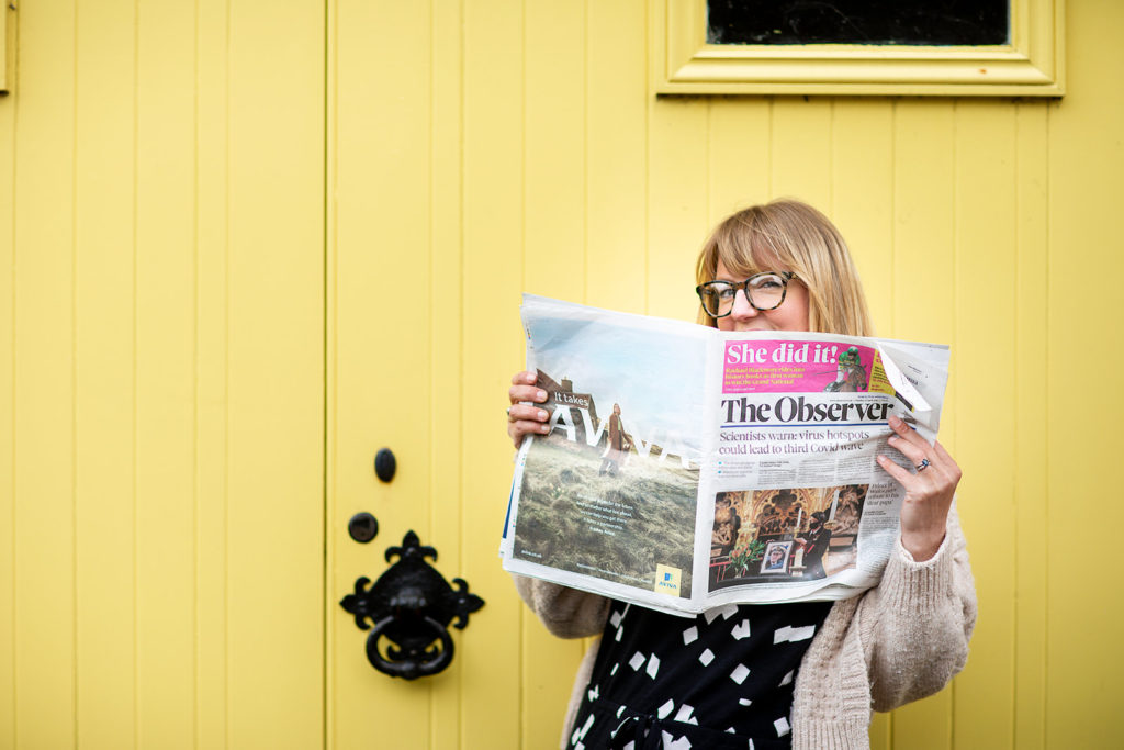 business woman is holding up a newspaper, standing in front of yellow door