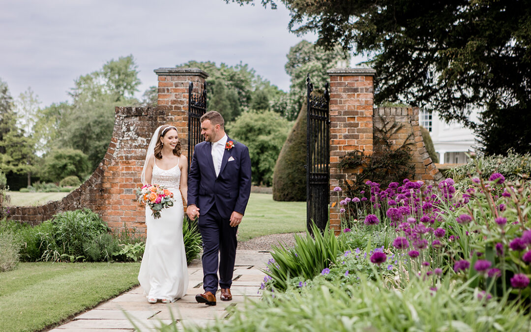 wedding couple at Essex venue, holding hands and walking on a walkway between flowers
